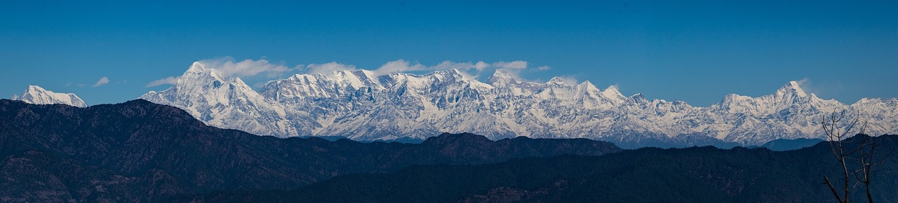 A wall of snow-covered Himalayan peaks seen from Ranikhet above blue hills